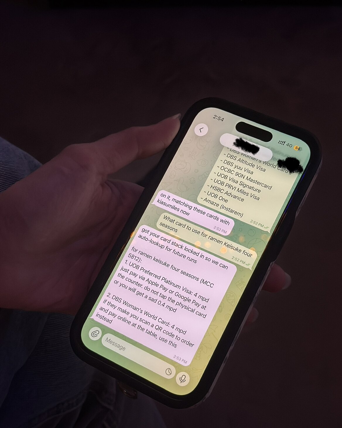 A person checking a KiasuMiles conversation on a phone at a restaurant